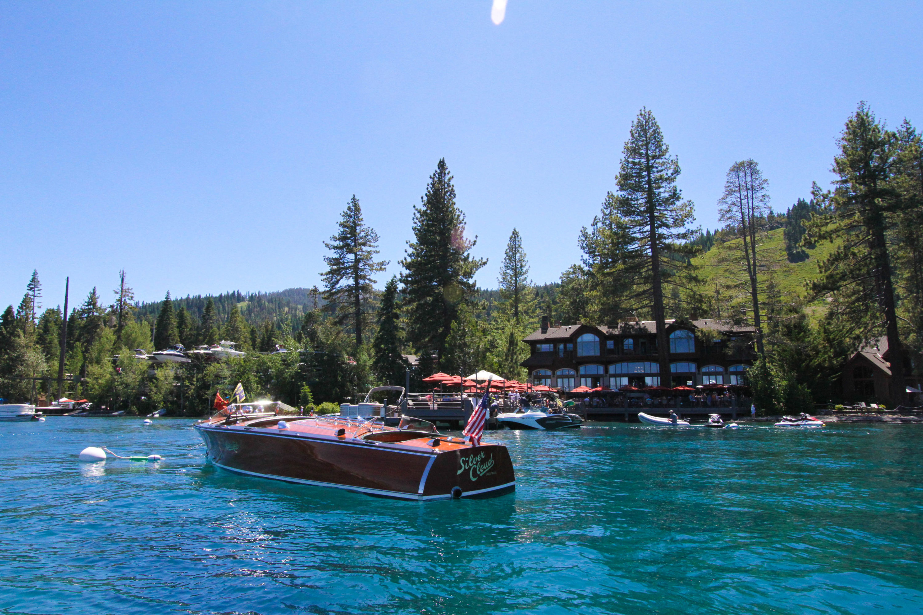 A wooden boat with the name "Silver Cloud" floats in front of West Shore Cafe on Lake Tahoe