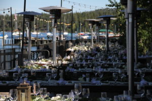 Dinner on the deck at West Shore Cafe Pier. There are wooden farm tables set with glassware and plateware.
