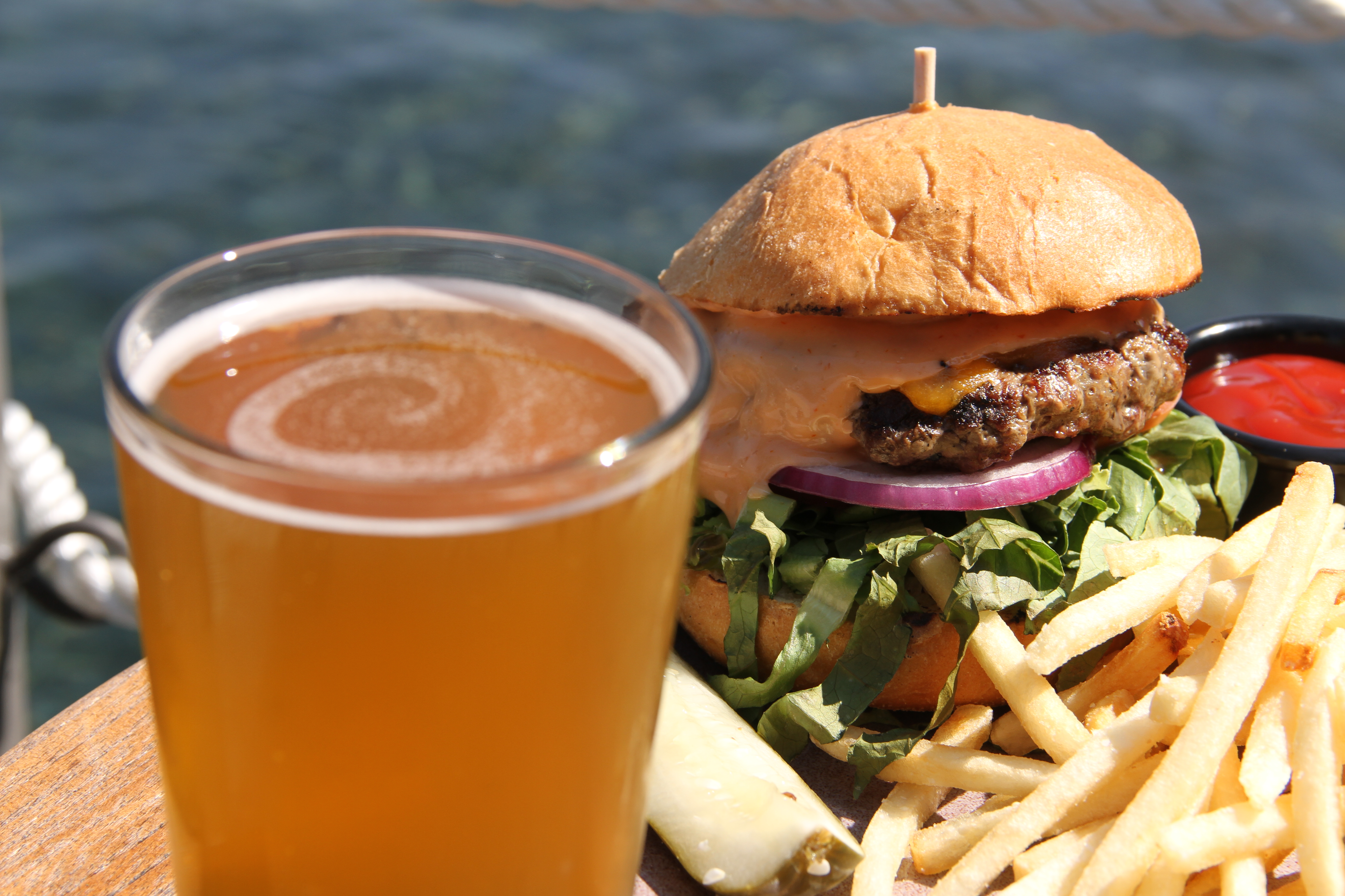 An up close photo shows a cheeseburger, fries and a beer.