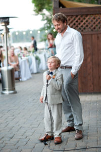 A young boy in a suit holds a microphone. An adult man stands behind him. Sandra Fazzino Photography