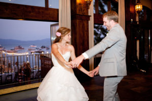 A bride and groom dance together in front of an open window. Lake Tahoe is outside the window.