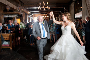 A bride and father dance togeter. People watch in the background.