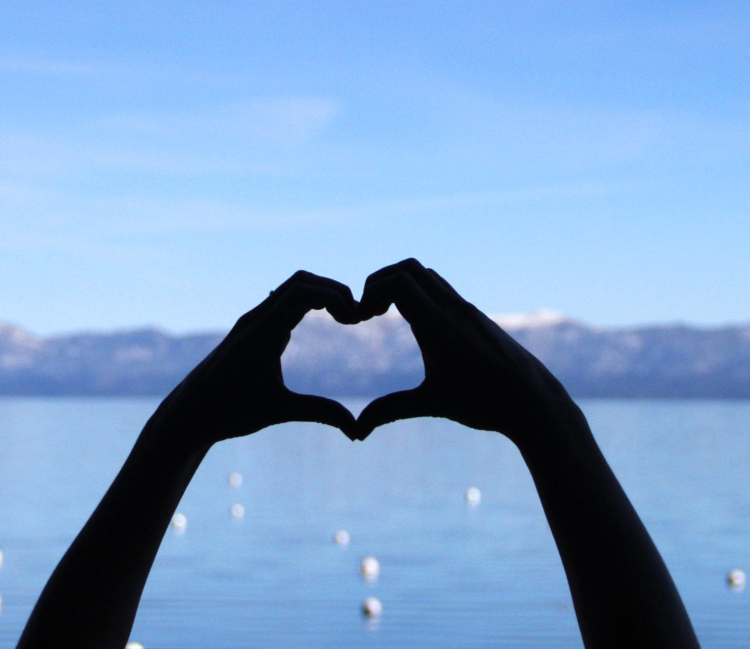 Two hands form a heart in front of Lake Tahoe.