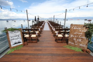 West Shore Cafe Pier is set for a wedding with chairs on either side of an aisle. Boats float on Lake Tahoe in the Background