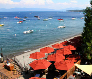 An overhead view shows the West Shore Cafe pier and deck. Boats tied to Buoys float on lake Tahoe in the background.