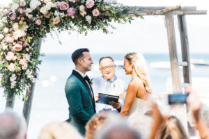 A Bride and Groom get ready to say "I do" under an alter with flowers. An officient stands behind them. Lake Tahoe is in the background. Custock Photography
