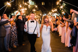 A Bride and Groom walk through a crowd at West Shore Cafe. The people in the crowd are waving sparklers Photography