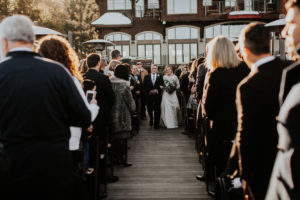 A bride and father walk down the aisle together on the West Shore Cafe Pier Kay Kroshus Photography