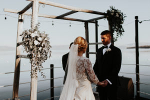 A bride and groom hold hands facing each other under an alter at the end of the West Shore Cafe Pier Kay Kroshus Photography